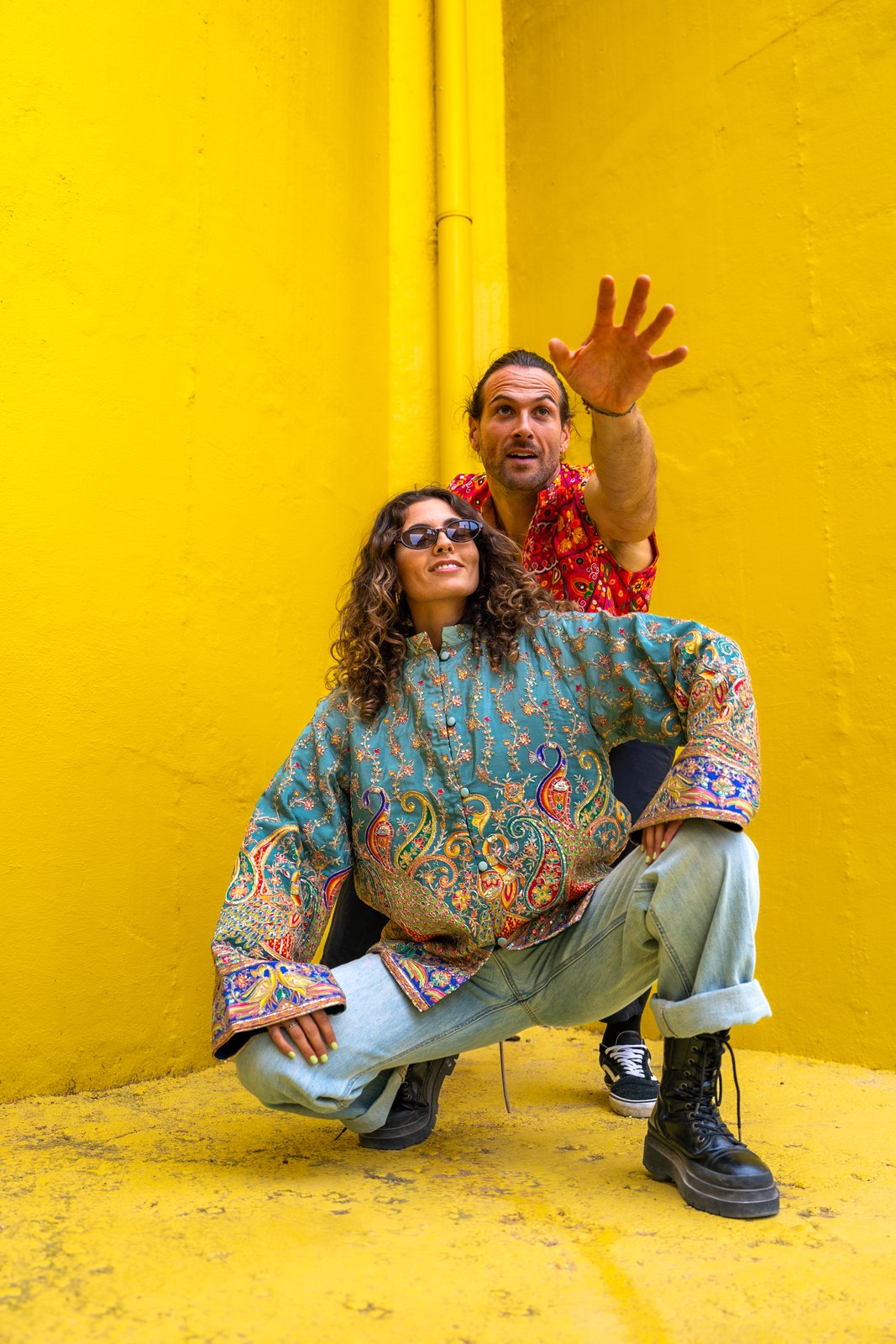 Two people in colourful clothes posing against a bright yellow wall