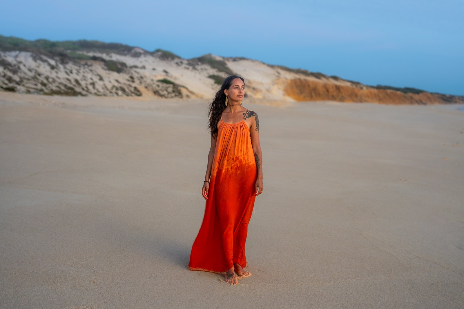 Woman in an orange dress on a wide sandy beach below dunes