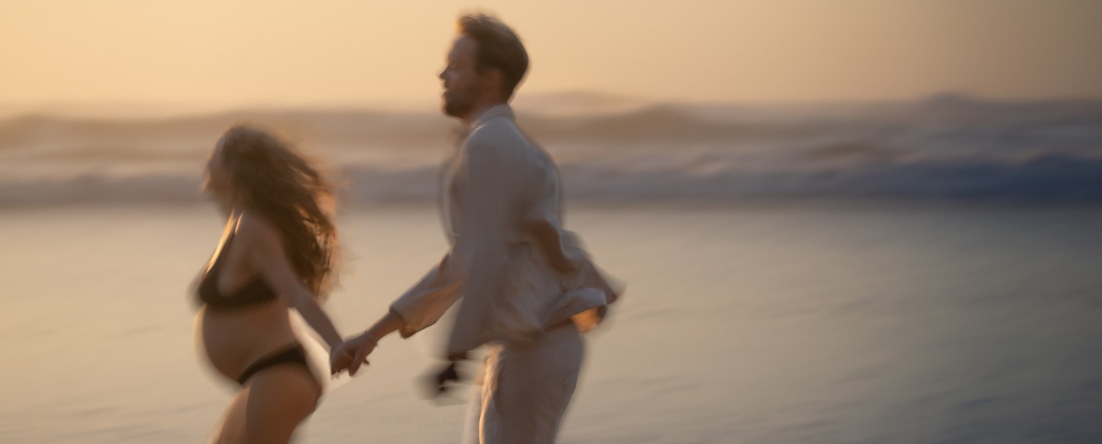 Couple walking hand in hand along the shore at golden hour